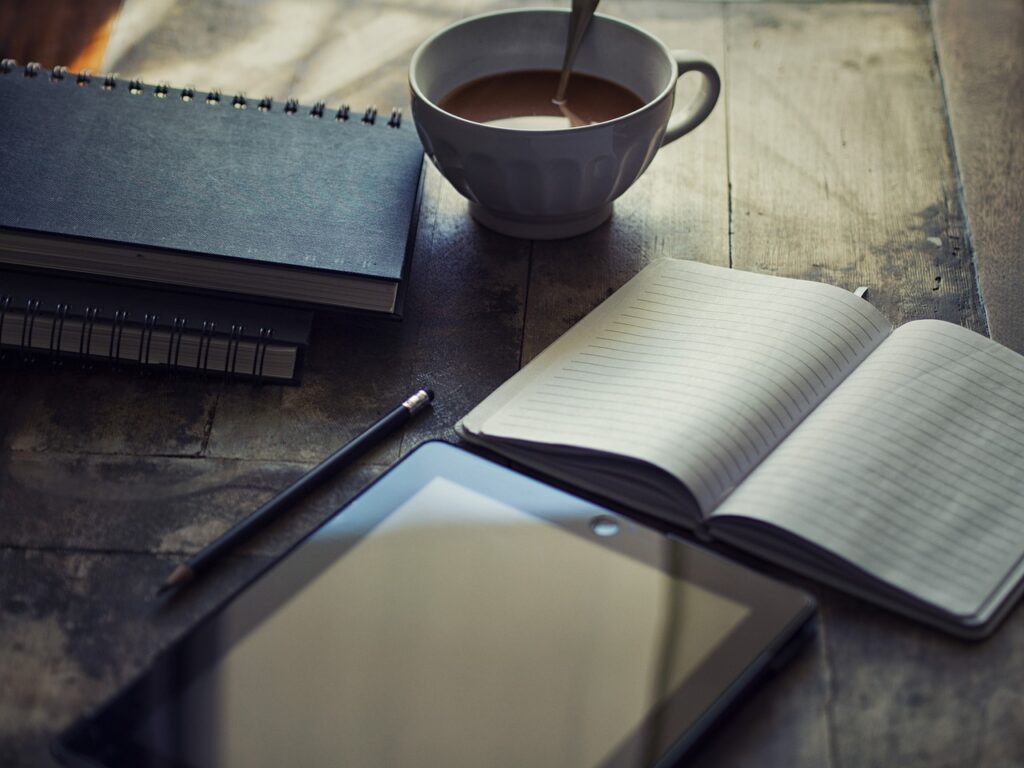 Notebook, coffee cup, and pen on a rustic wooden table, representing a fresh start and personal reflection.